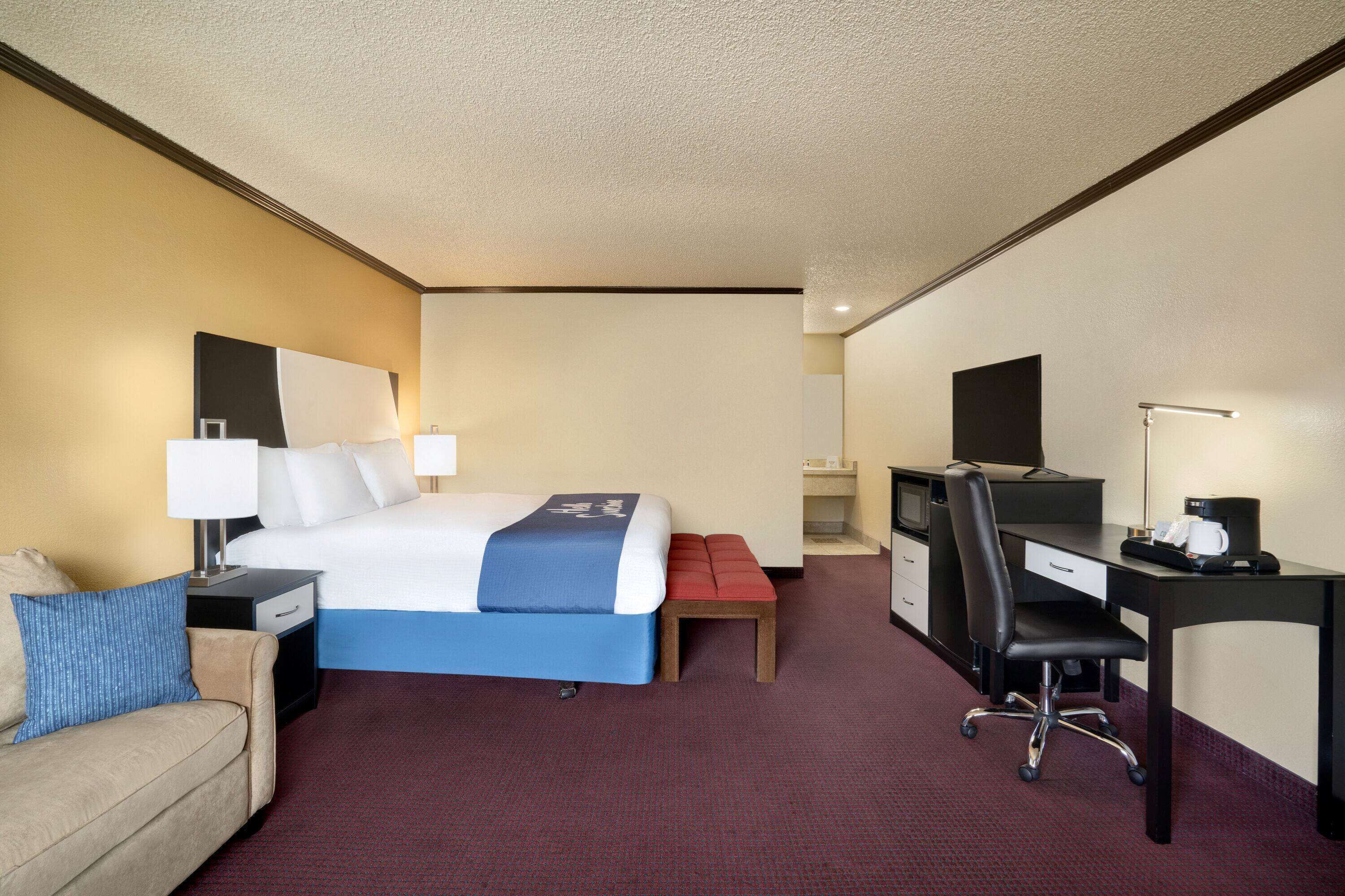 A hotel room with a bed, a desk, a chair, a television, and a sofa.