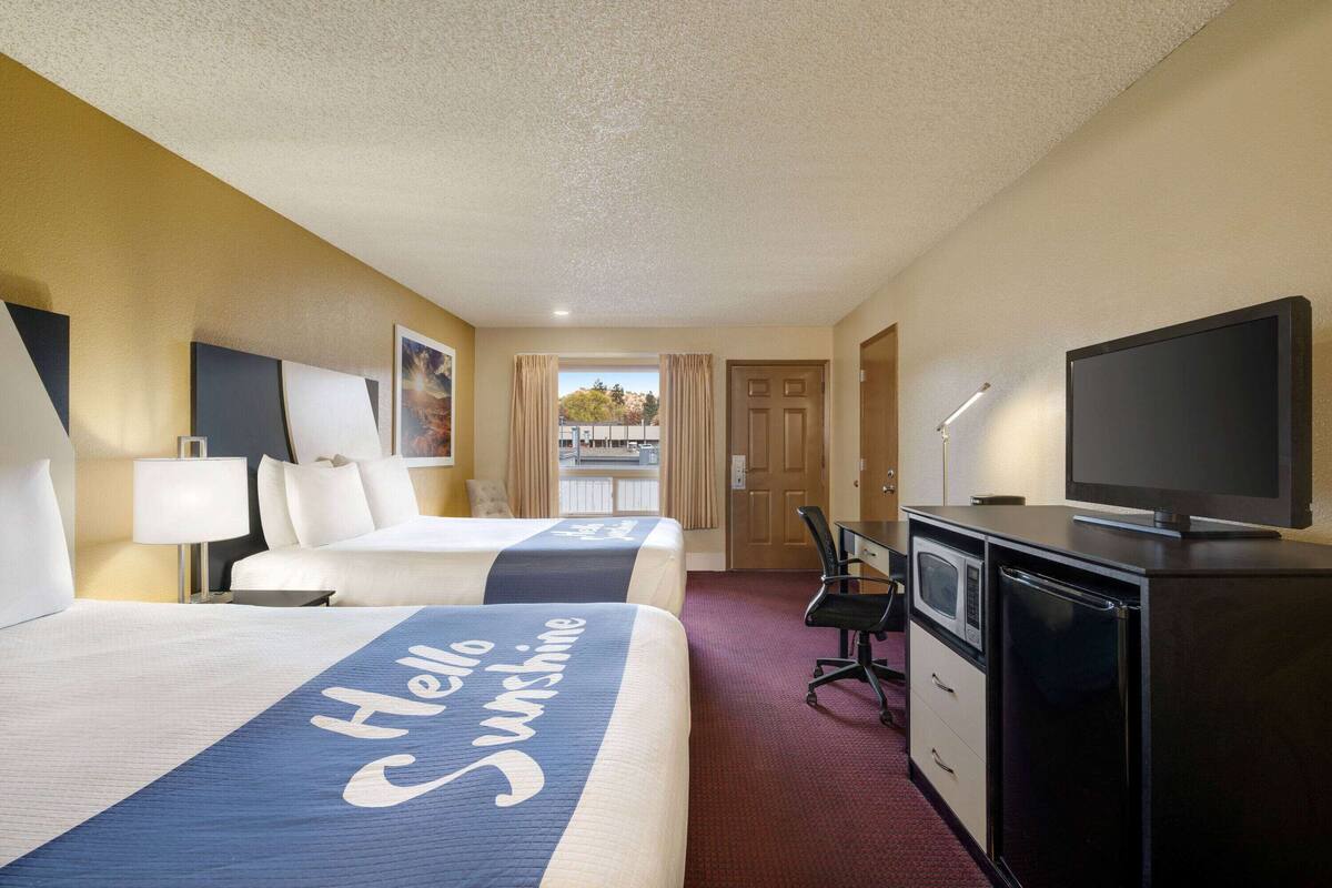 A hotel room with two beds, a desk, a television, and a view of the outside.