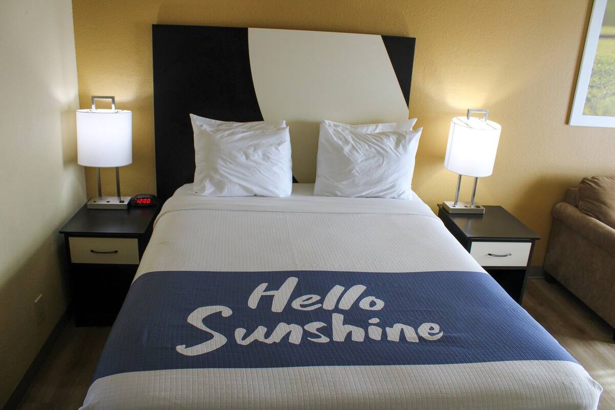 A hotel room with a bed, two bedside tables, a nightstand, a lamp, and a couch.