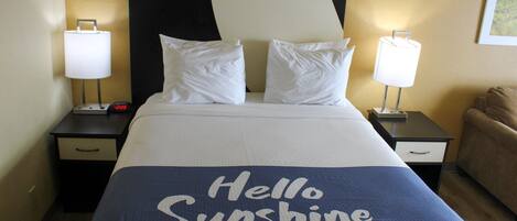 Quarto de hotel com cama, duas mesas de cabeceira, um criado-mudo, abajur e um sofá.