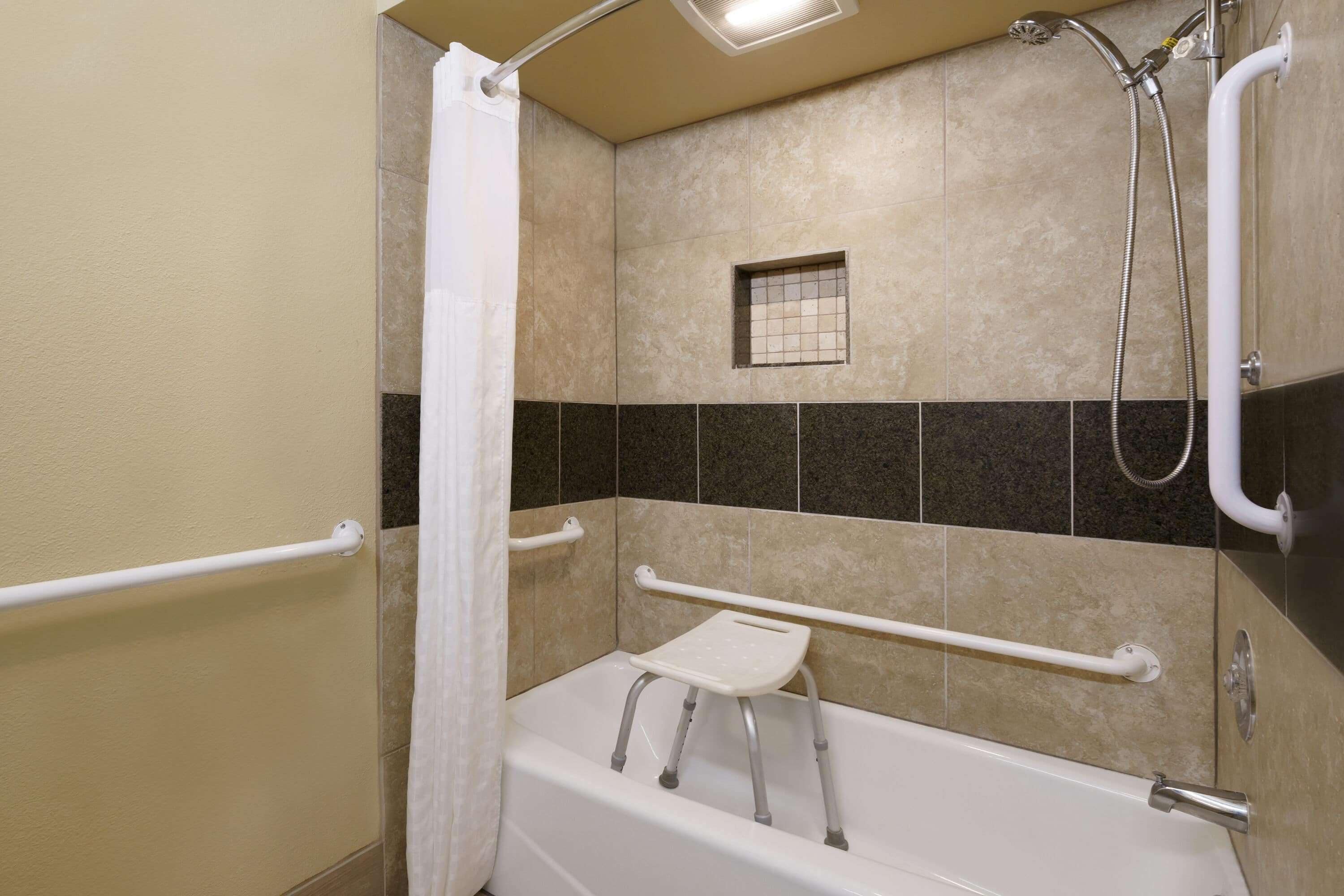 A bathroom with a bathtub, grab bars, and a shower head.