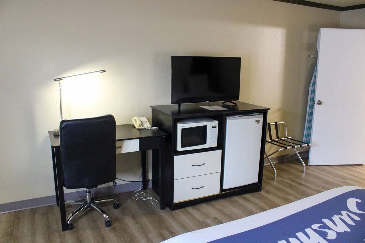 A hotel room with a desk, a chair, a television, a microwave, a refrigerator, and a bed.