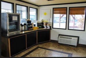 A kitchen with a built-in microwave, a coffee machine, and a small refrigerator. There are large windows providing natural light and a view of the outside.