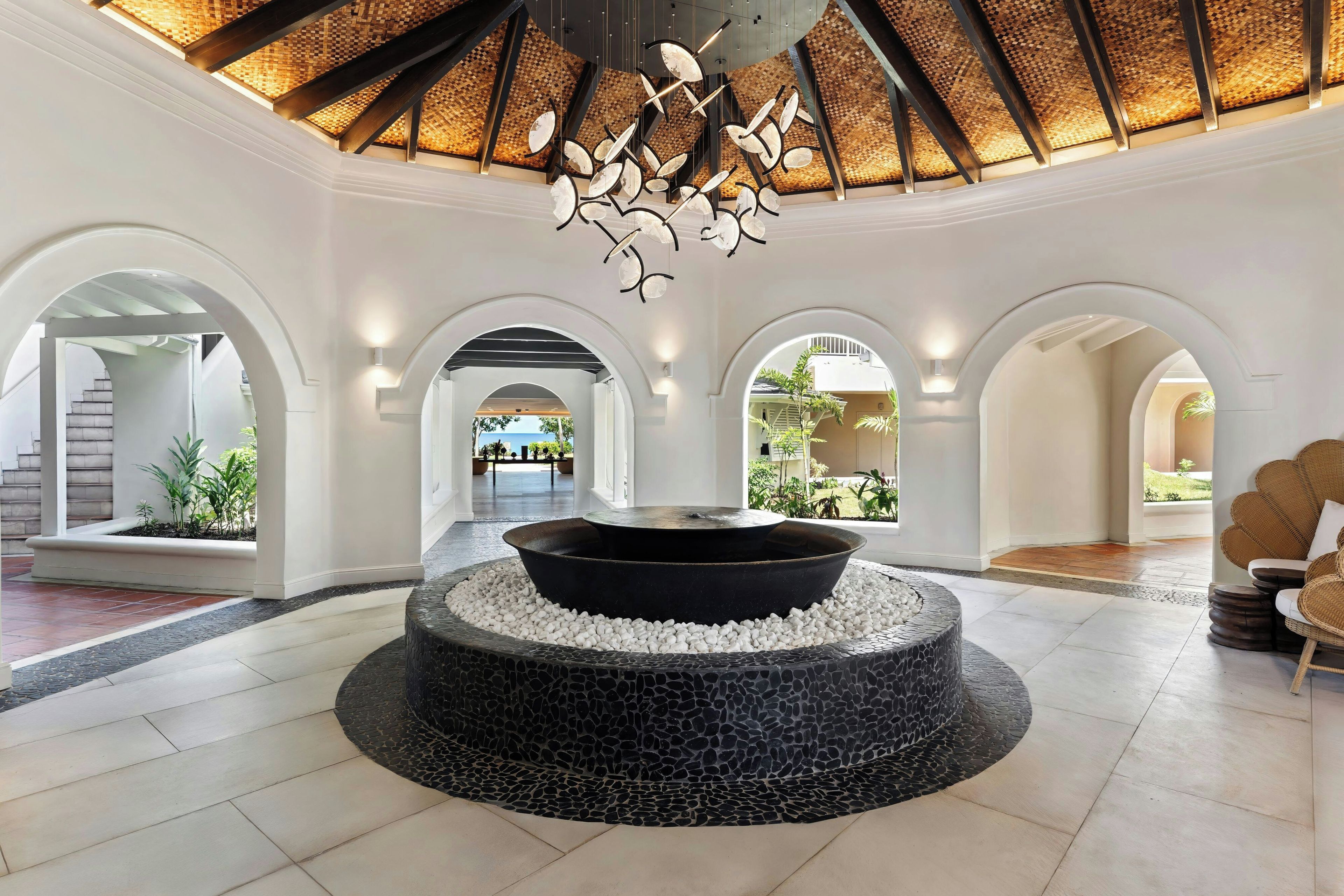 A spacious lobby with a central fire feature, arched doorways, and a ceiling with a woven pattern.