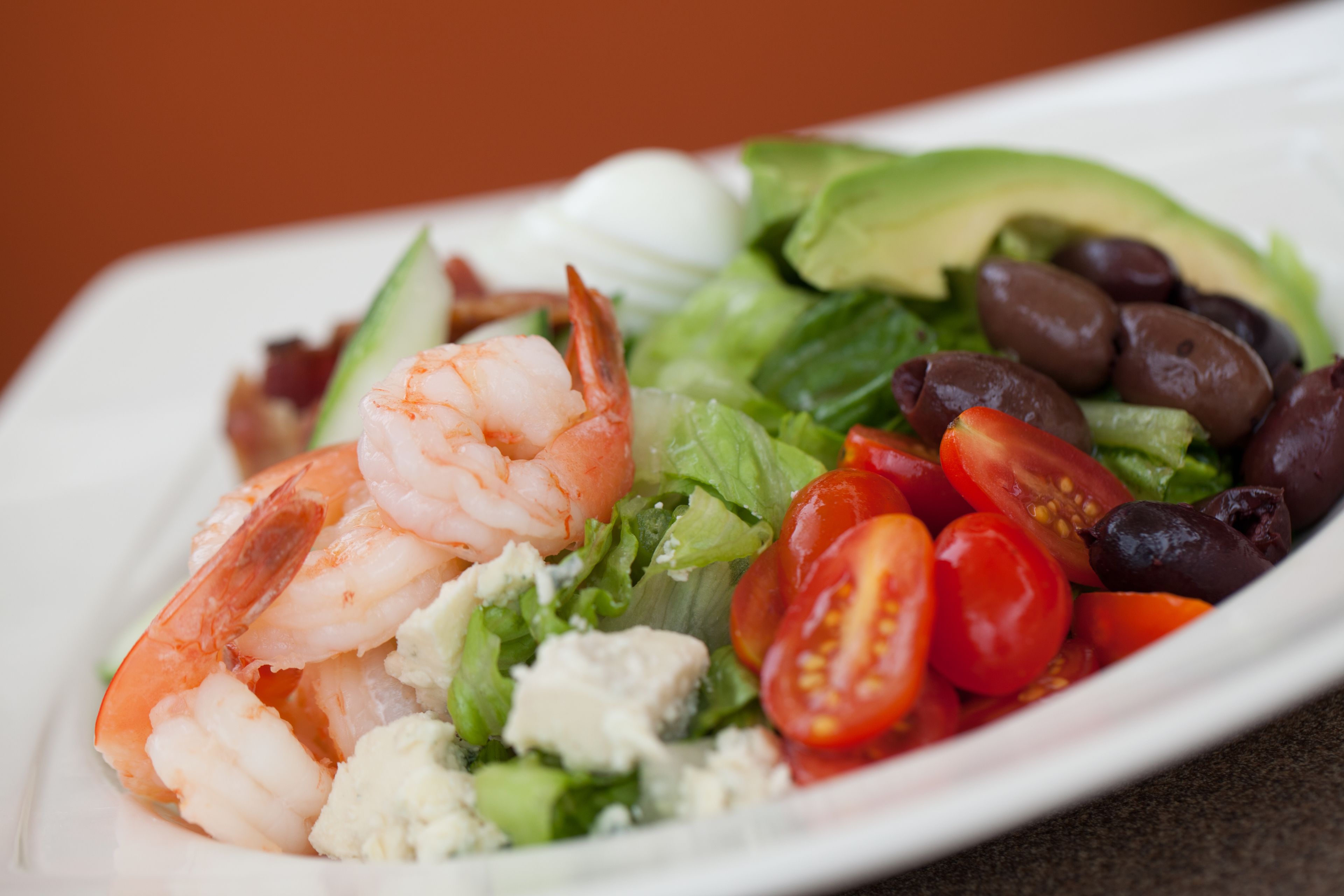 A plate of shrimp, avocado, tomatoes, olives, and feta cheese.