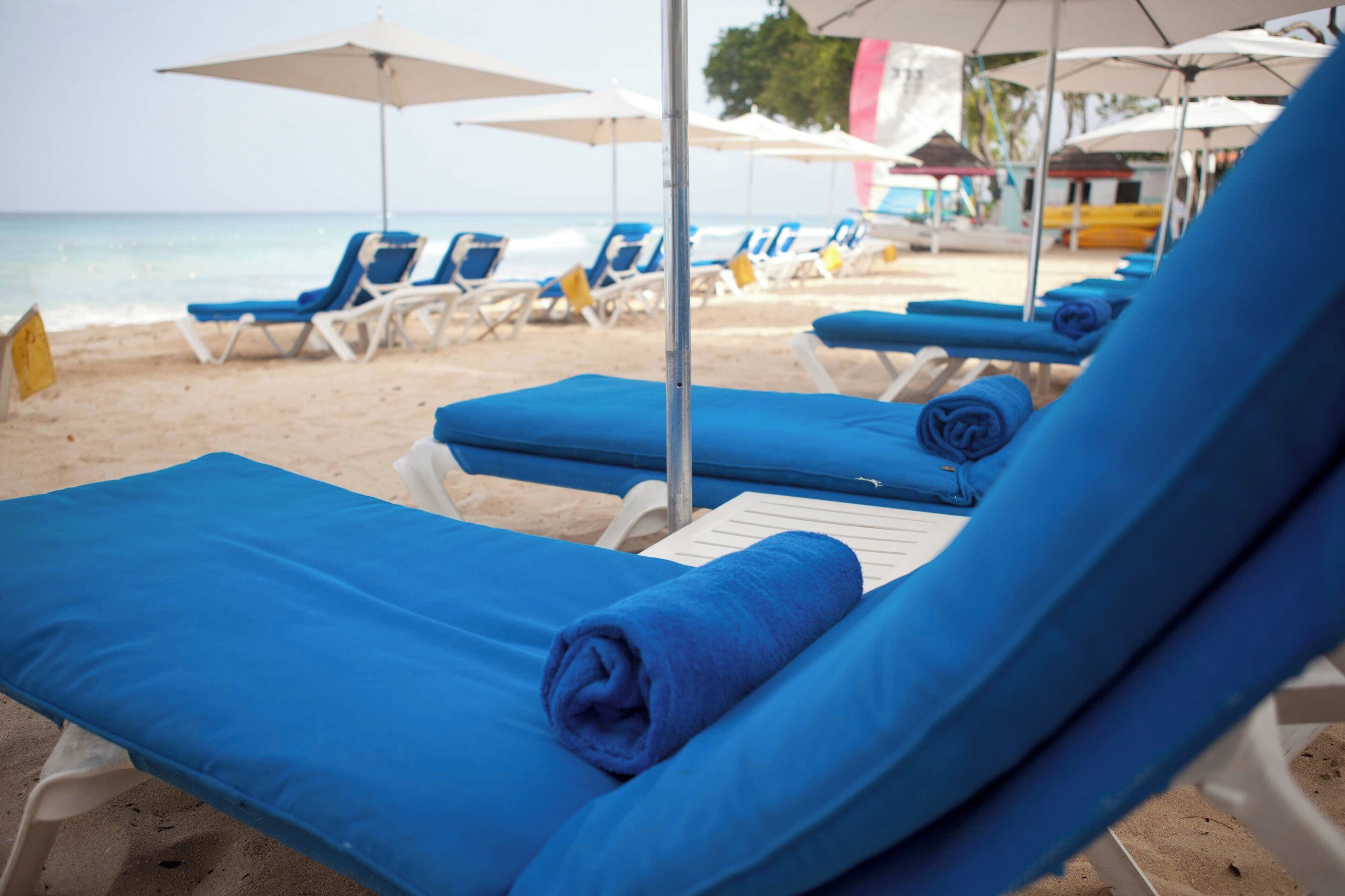 Un área de descanso en la playa con sillones azules y sombrillas blancas.