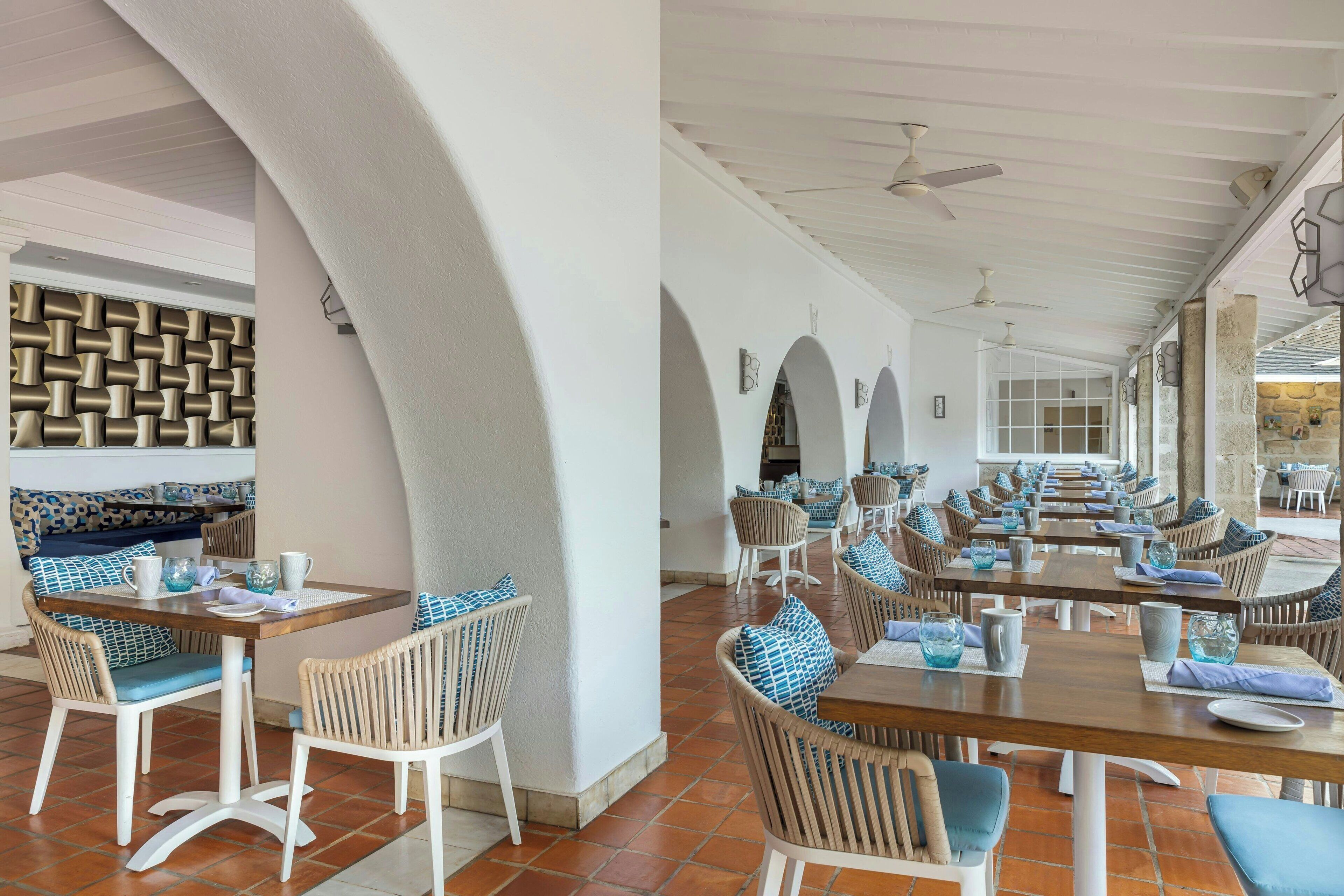 Un restaurant avec des chaises en osier blanc et marron, des coussins bleus et un sol carrelé.