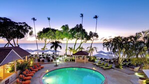 A poolside area with lounge chairs and umbrellas, surrounded by palm trees and a view of the ocean. - Tamarind, Barbados, An Autograph Collection® All-Inclusive Resort (Paynes Bay)