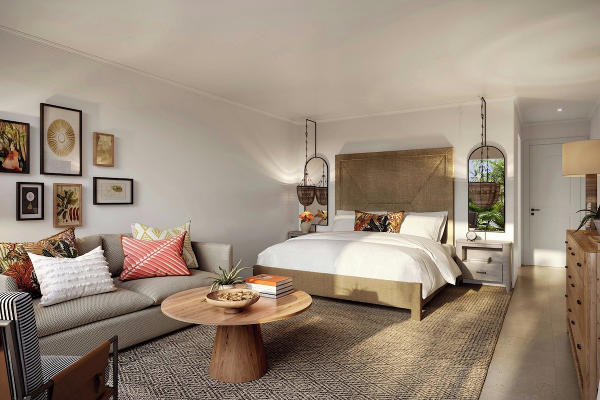 A modern bedroom with a bed, sofa, round coffee table, and artwork on the walls.