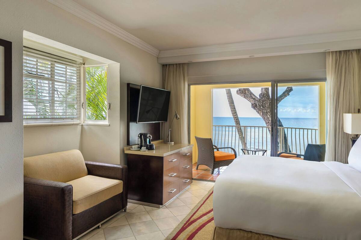 Une chambre d’hôtel comprenant un lit, un canapé, un bureau avec une télévision et un balcon avec vue sur la mer.