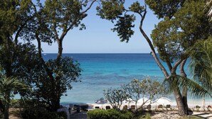 A beach view with trees, a clear sky, and a calm sea. - Tamarind, Barbados, An Autograph Collection® All-Inclusive Resort (Paynes Bay)