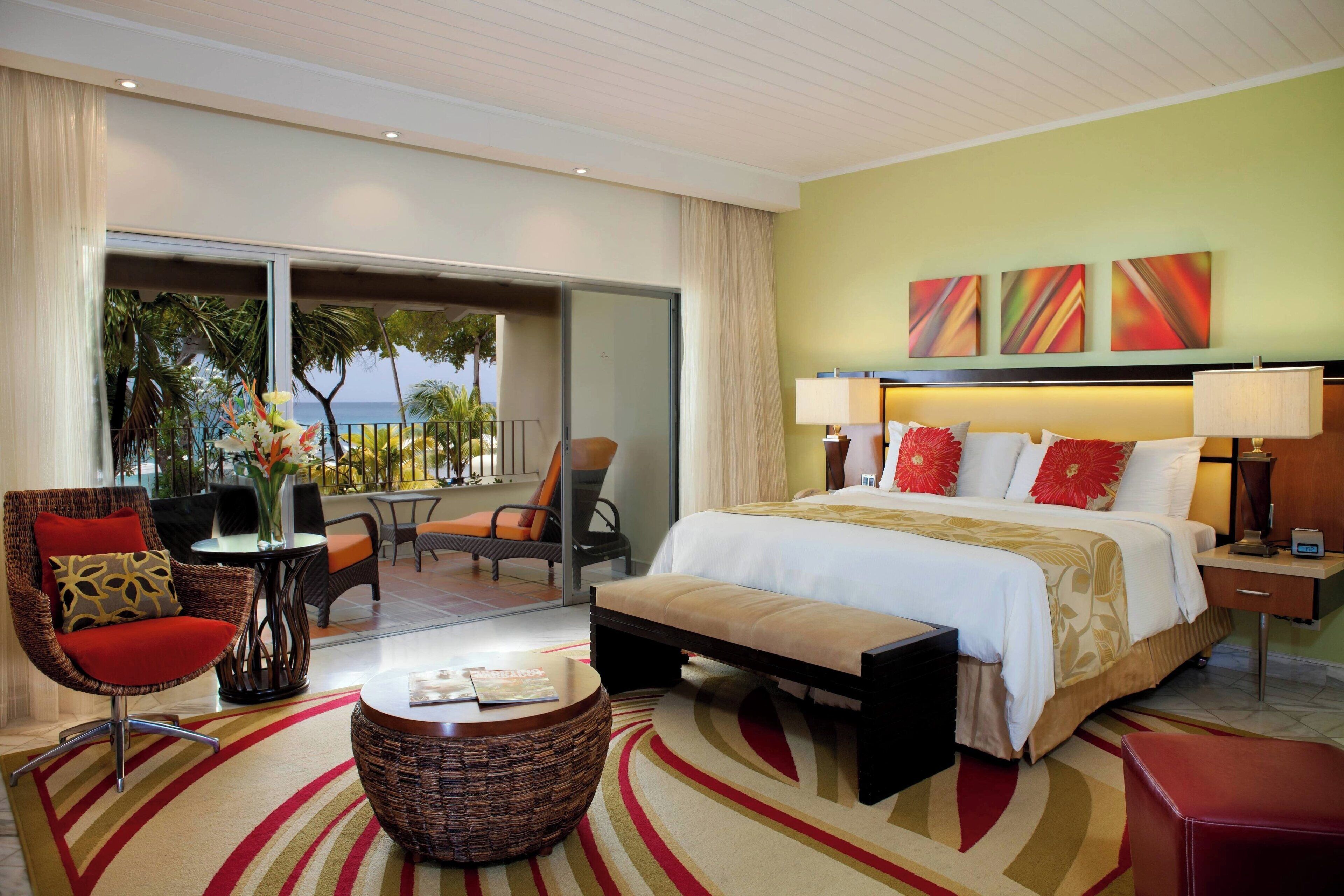 Une chambre d’hôtel dotée d’un grand lit, d’un coin salon avec un fauteuil et une table, et offrant une vue sur l’océan grâce à une porte coulissante.
