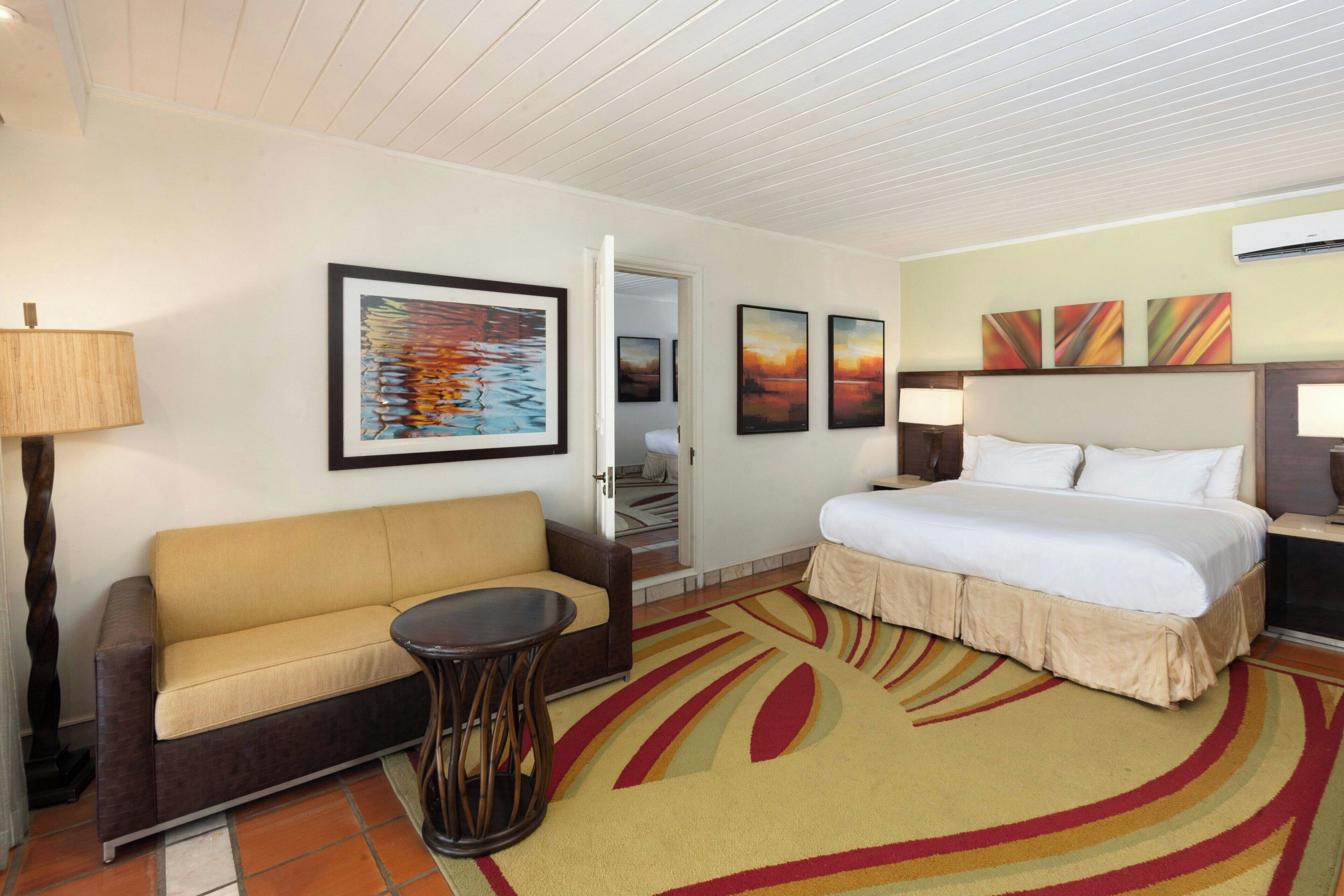 A hotel room with a bed, a sofa, a small table, and artwork on the walls.