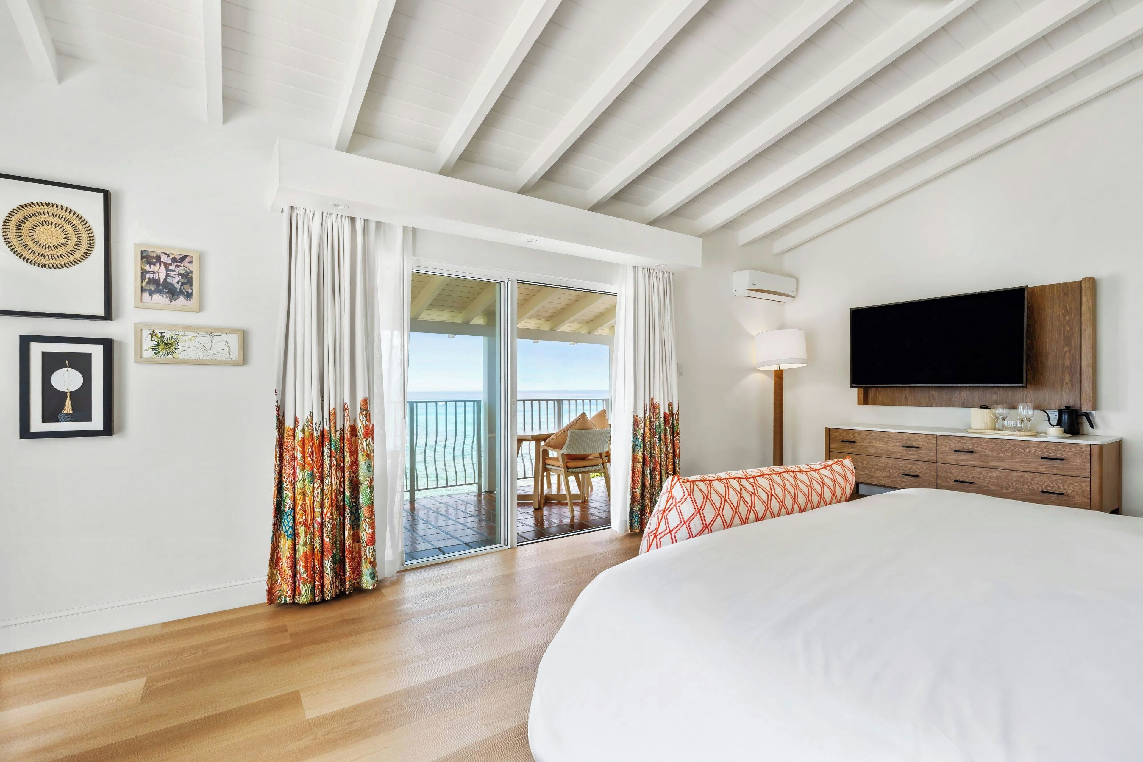 A hotel room with a large bed, a TV, a wooden dresser, and a balcony with curtains.