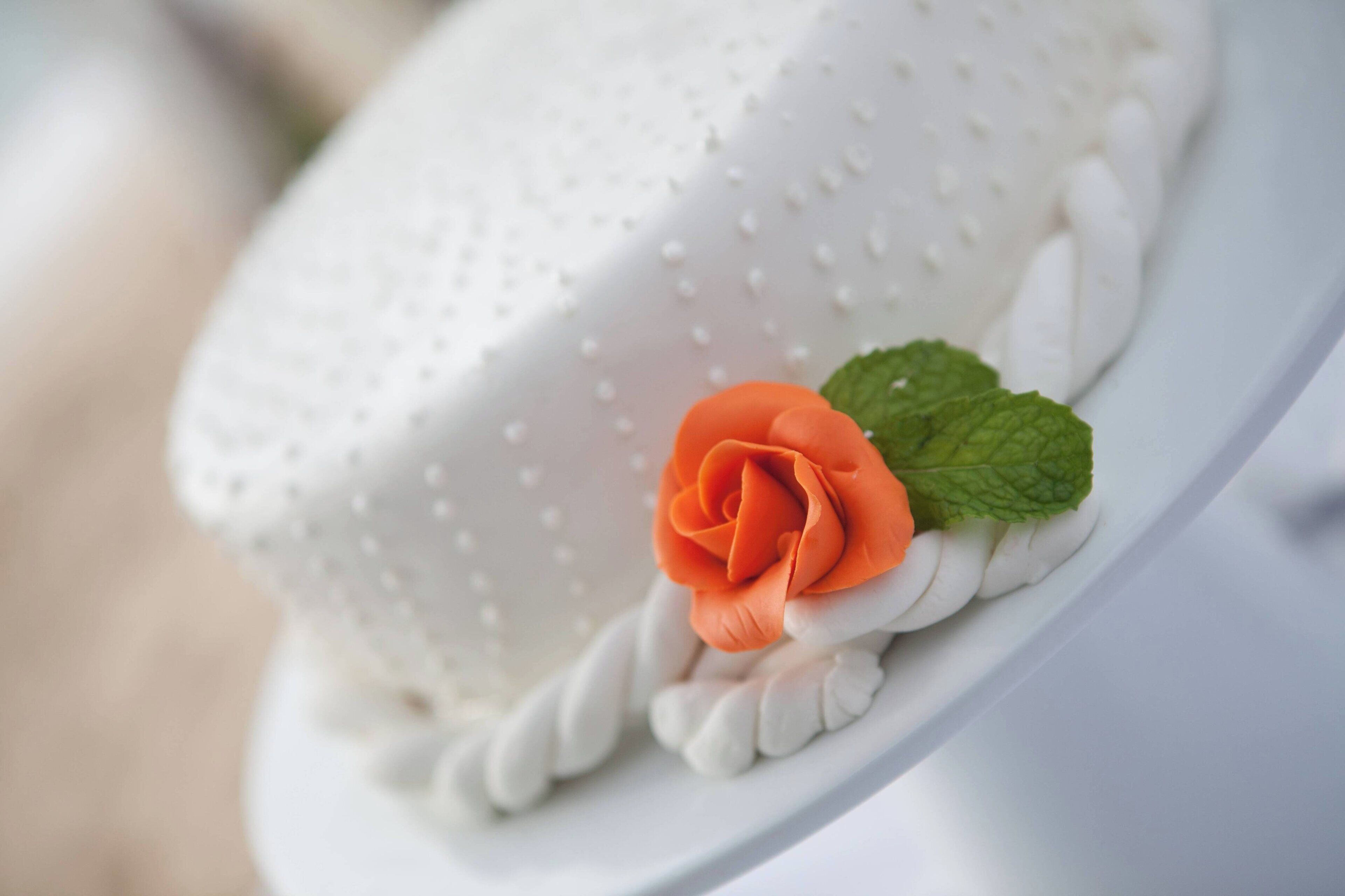 Un gâteau à la surface blanche et texturée, orné d’une seule fleur orange et de feuilles vertes.
