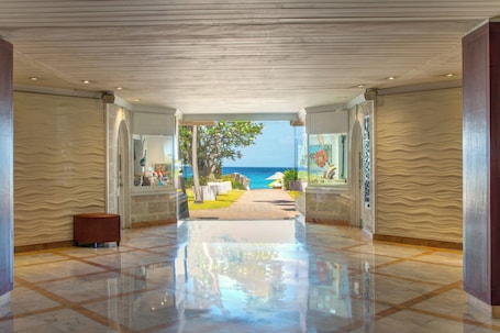 A spacious lobby with a polished floor, a view of the sea, and a pathway leading to outdoor seating.