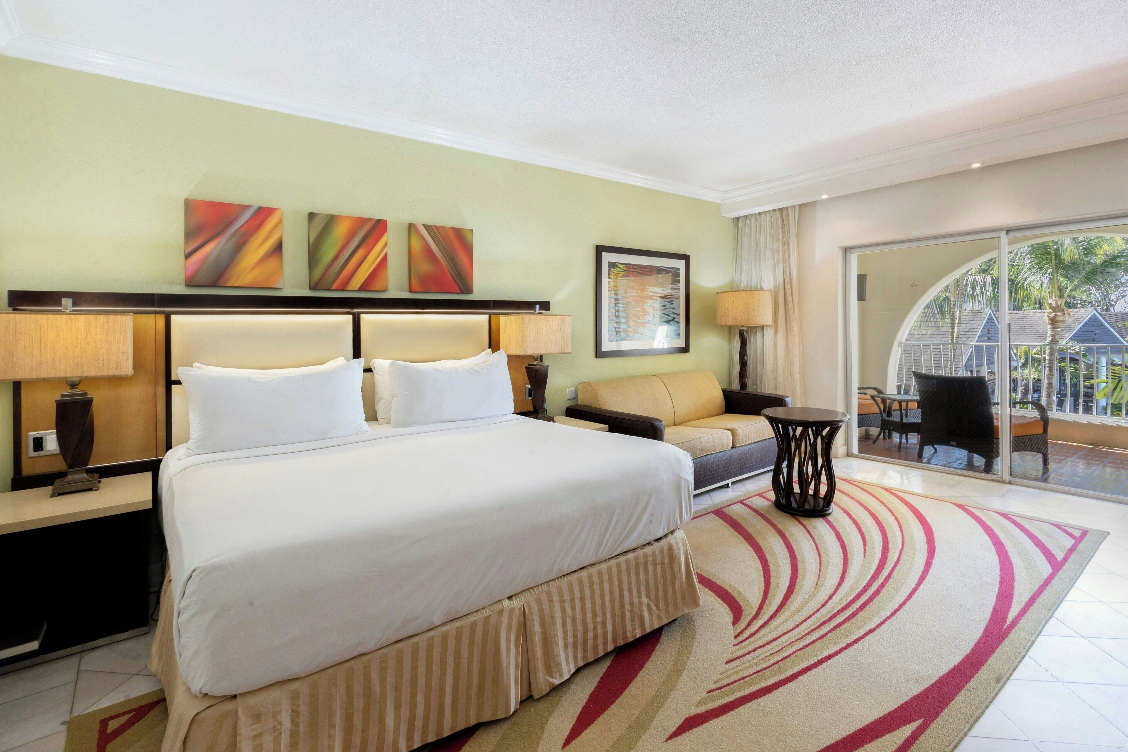 Ein Hotelzimmer mit einem großen Bett, einer Couch, einem kleinen Tisch und Blick ins Freie durch eine Schiebetür.