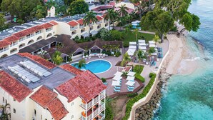 An aerial view of a resort with a swimming pool, beach, and multiple buildings with red-tiled roofs. - Tamarind, Barbados, An Autograph Collection® All-Inclusive Resort (Paynes Bay)