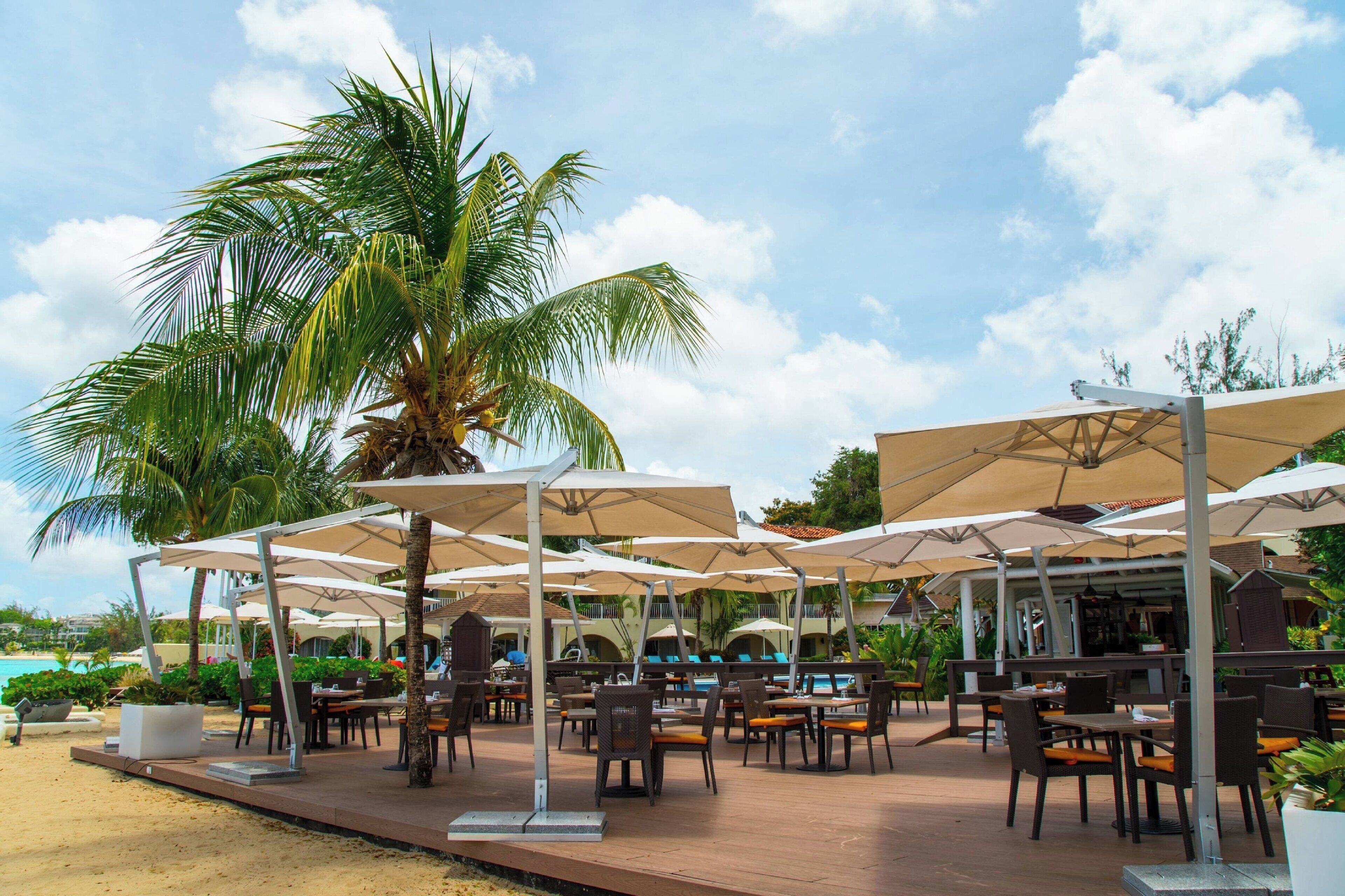 An outdoor dining area with umbrellas, tables, and chairs, overlooking a pool and beach.
