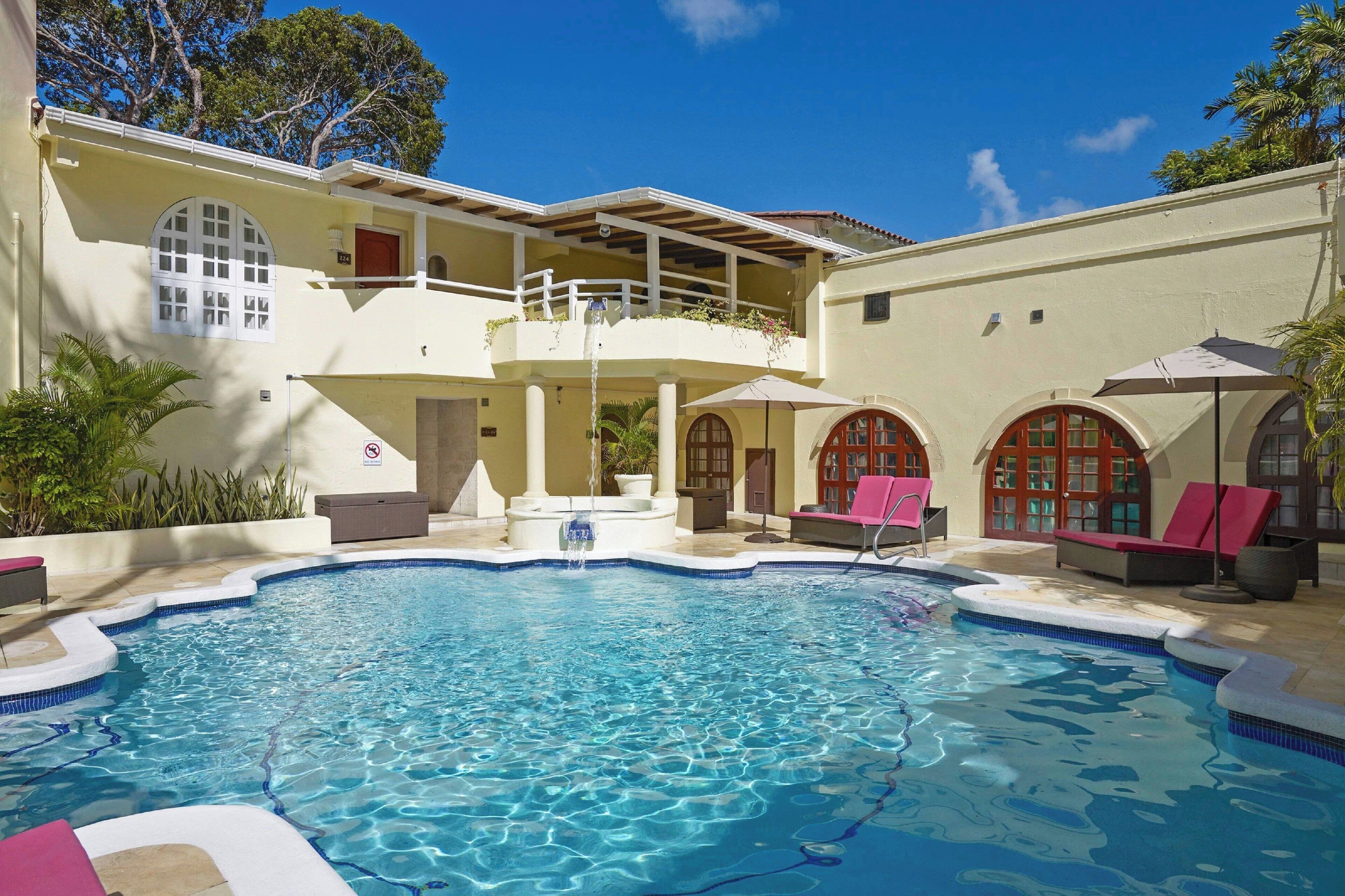 A swimming pool with a sun terrace, lounge chairs, and a covered seating area.
