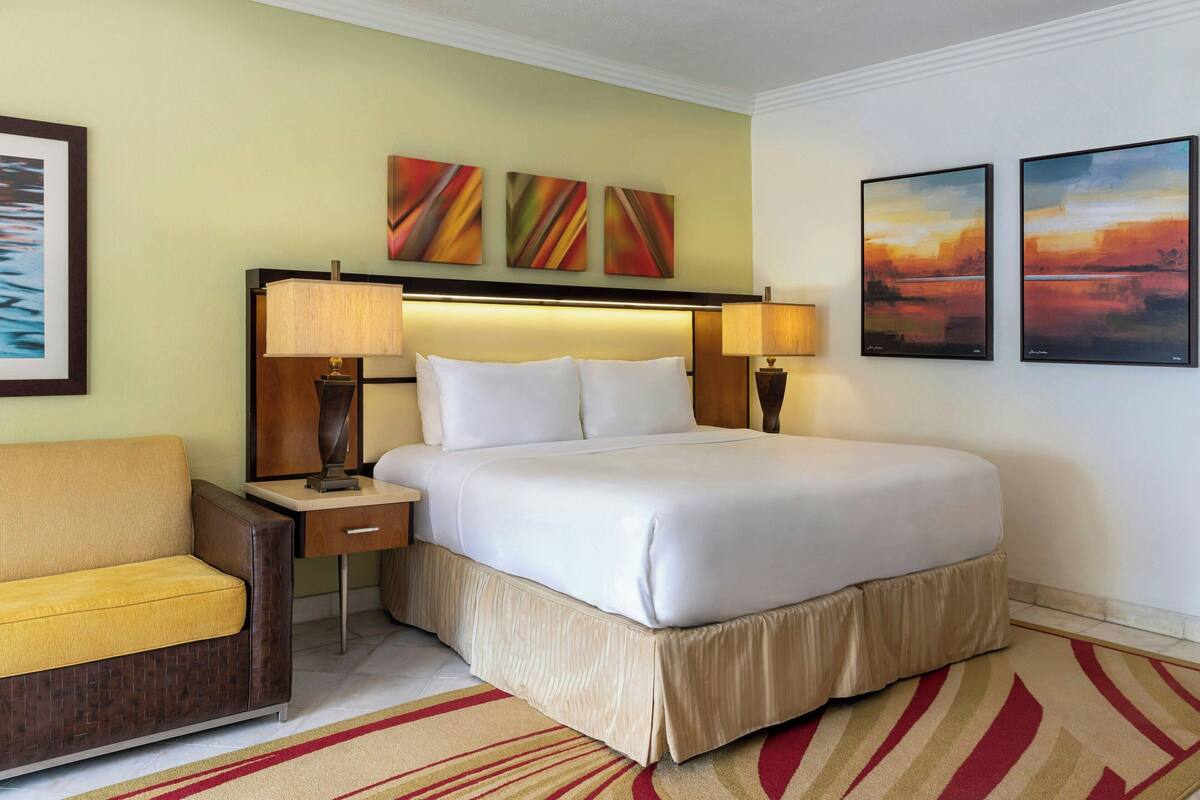 Une chambre d’hôtel avec un lit, des tables de chevet, une chaise et des œuvres d’art accrochées aux murs.