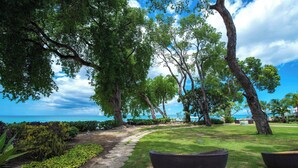 A garden with a stone pathway, lush greenery, and large wicker chairs. - Tamarind, Barbados, An Autograph Collection® All-Inclusive Resort (Paynes Bay)