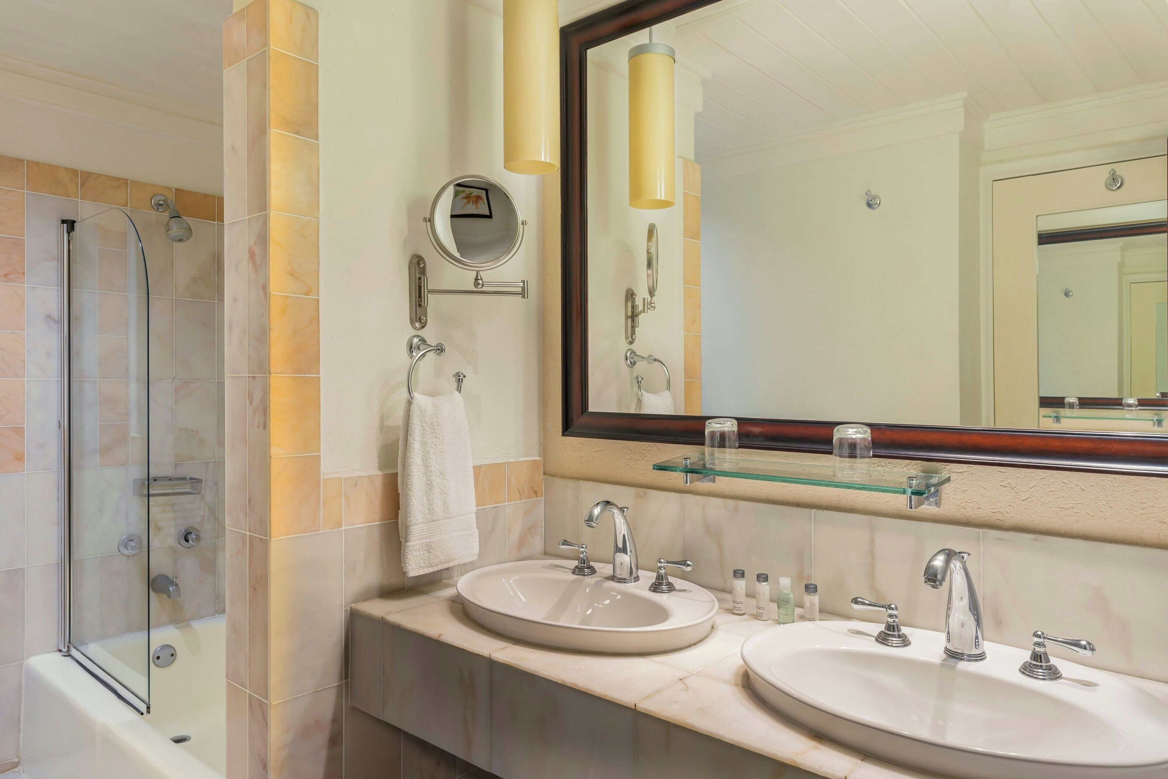 A bathroom with two sinks, a mirror, and a glass-enclosed shower.