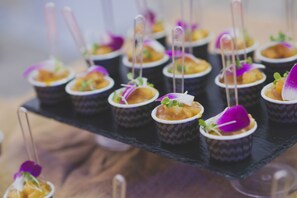 Una bandeja negra con varias tazas pequeñas de comida adornada con flores moradas y hojas verdes.