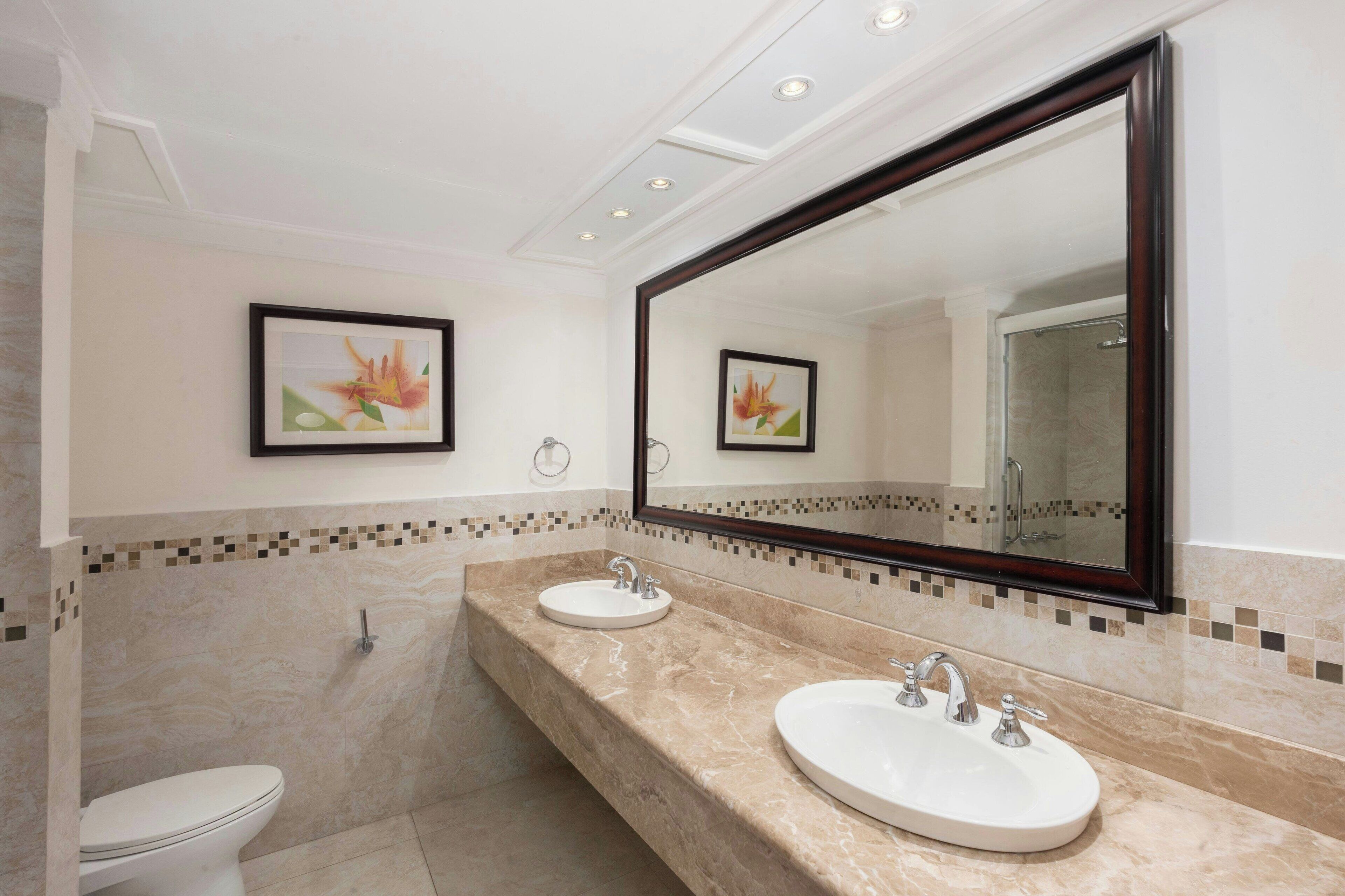 A bathroom with two sinks, a toilet, and a large mirror.