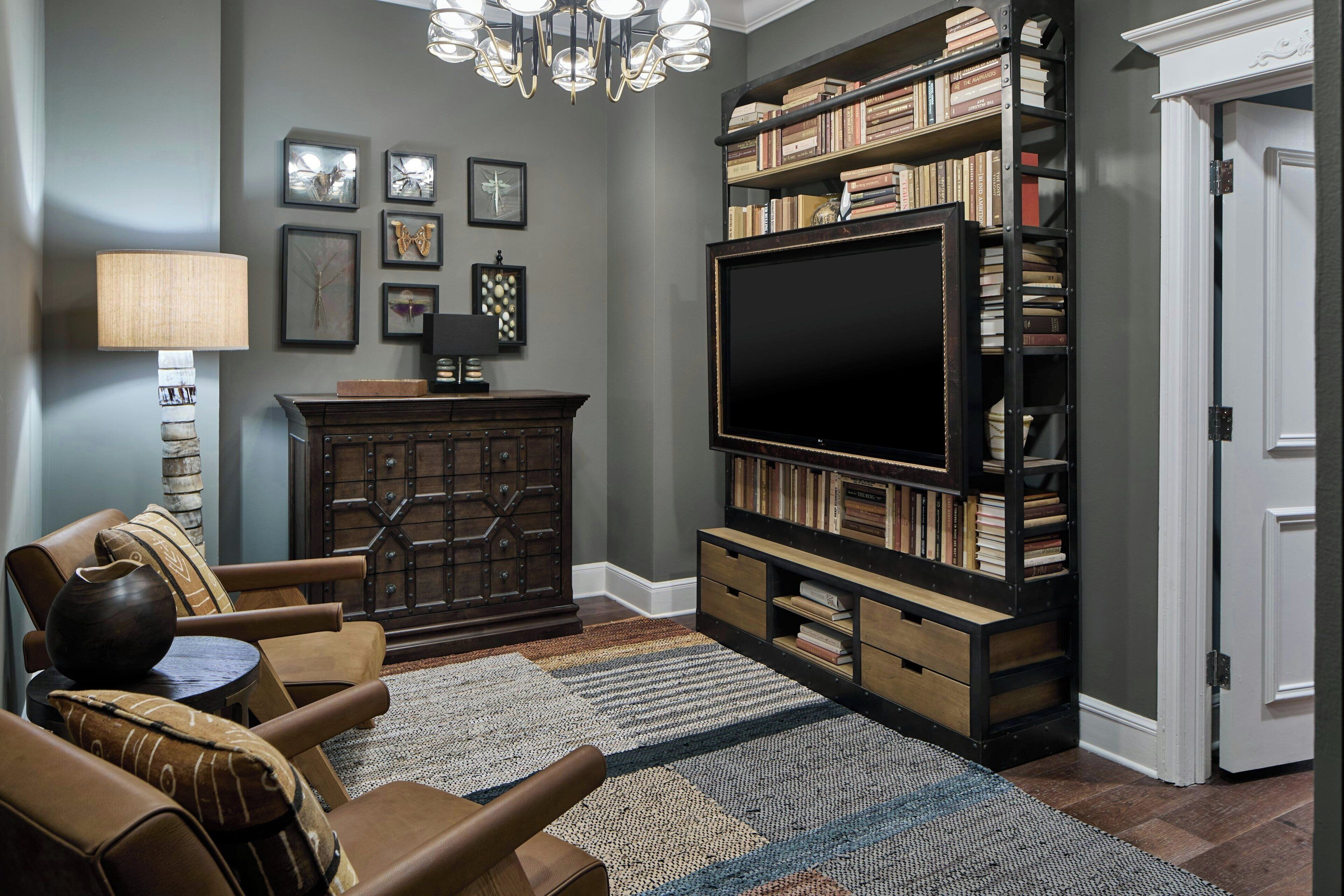 A living room with a large flat-screen TV, a bookshelf, leather armchairs, and a patterned rug.