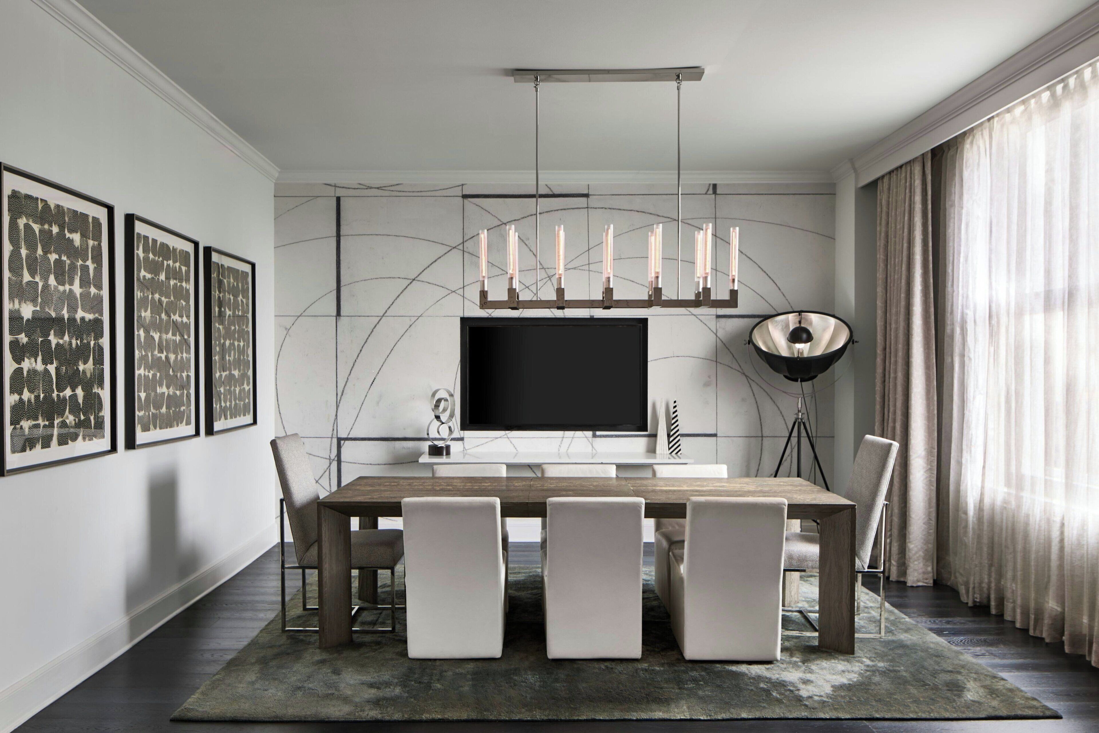 Une salle à manger moderne avec un grand téléviseur à écran plat, une table à manger en bois et quatre chaises. Les murs sont ornés d’œuvres d’art encadrées et une lampe sur pied se trouve dans la pièce.
