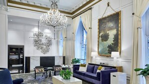 A spacious living room with a large chandelier, a fireplace, a sofa set, and a large painting on the wall. - Le Pavillon, New Orleans, a Tribute Portfolio Hotel by Marriott (New Orleans)