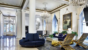 A spacious lobby with a grand chandelier, a blue sofa, and a patterned ottoman. - Le Pavillon, New Orleans, a Tribute Portfolio Hotel by Marriott (New Orleans)