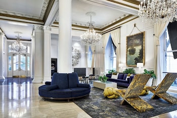 A grand lobby with a large chandelier, ornate columns, a fireplace, and seating arrangements. at Le Pavillon, New Orleans, a Tribute Portfolio Hotel by Marriott