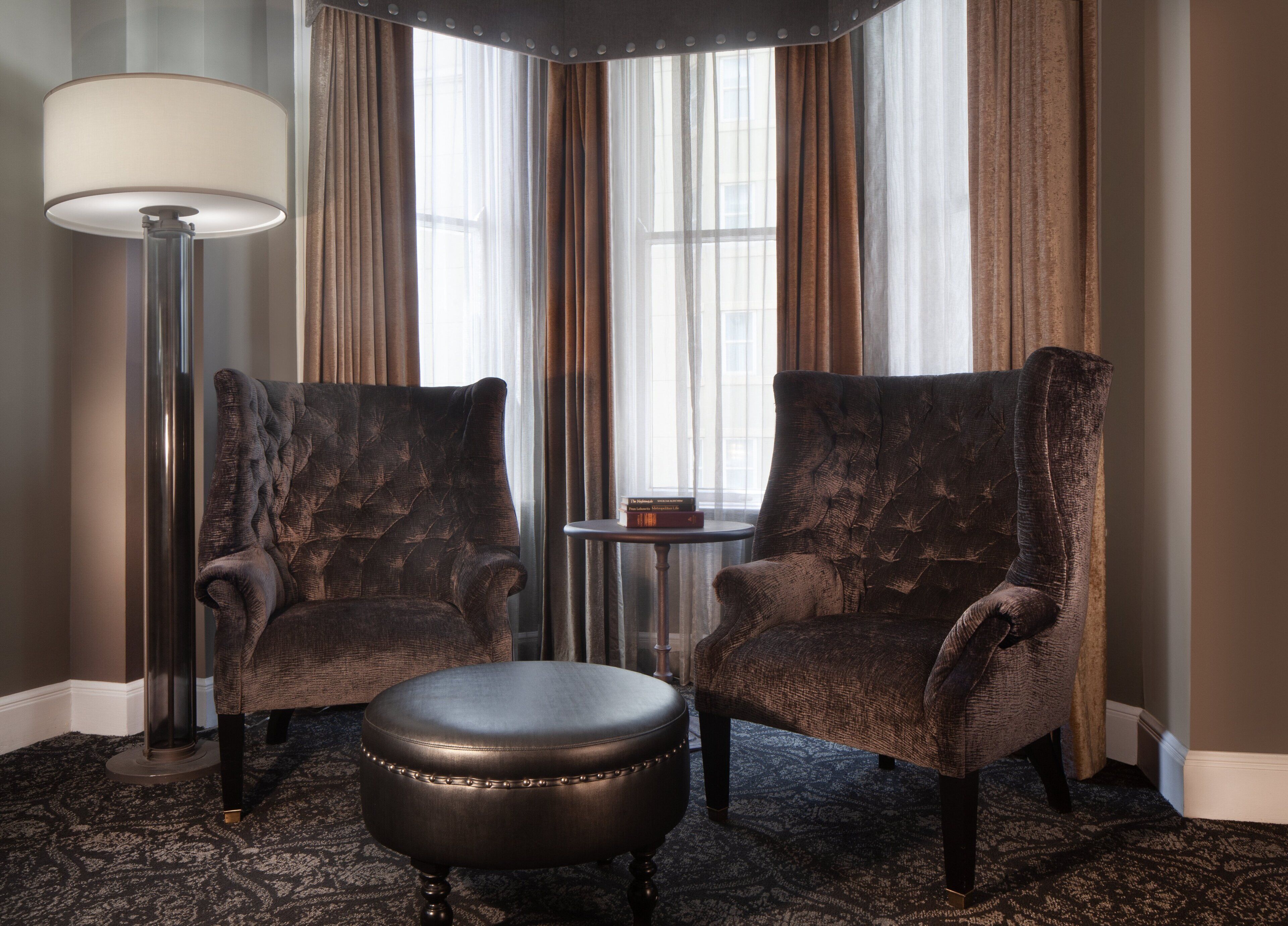 A room with two armchairs and a small ottoman, a floor lamp, and a side table with books.