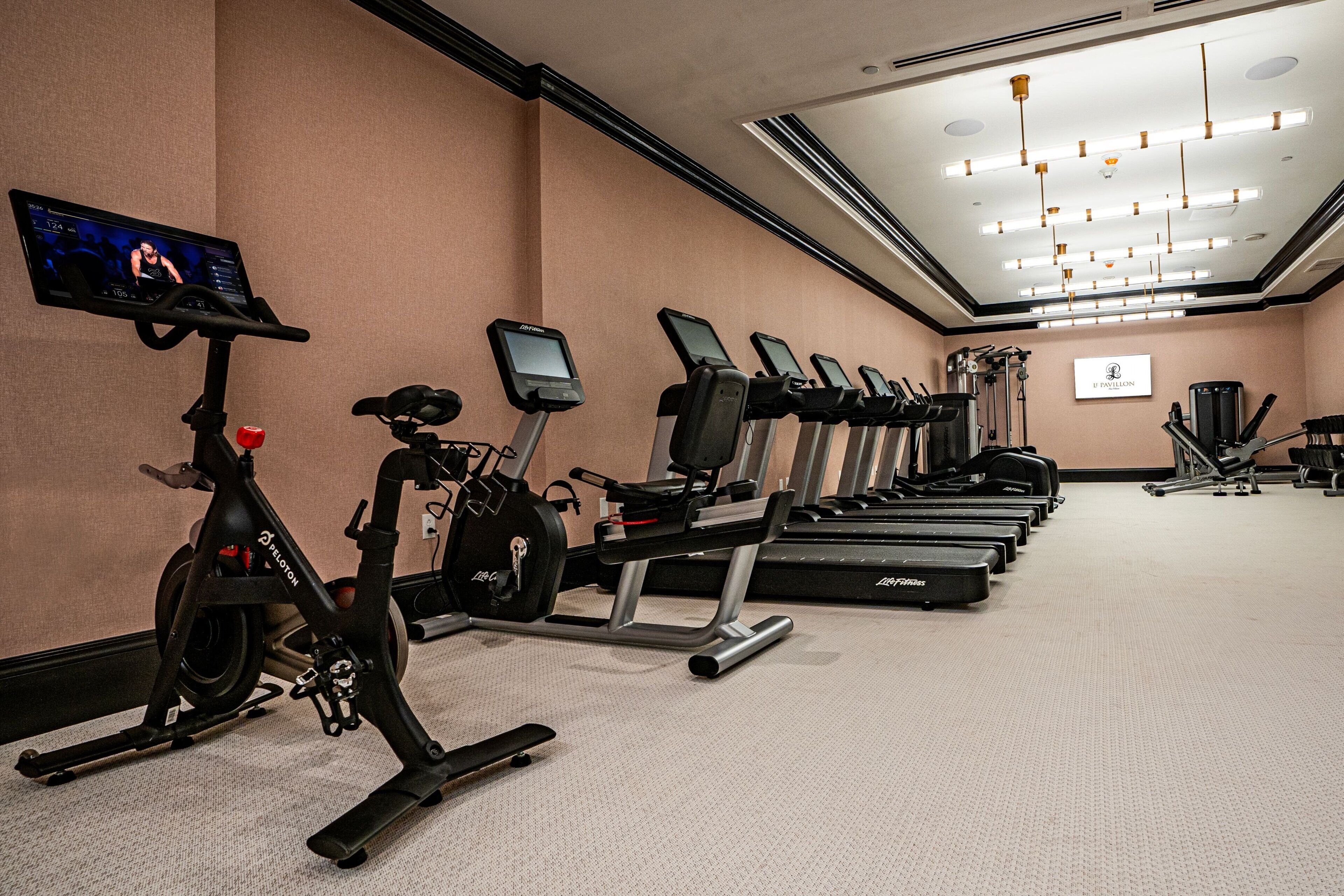 A gym with stationary bikes, treadmills, and a television screen displaying a workout program.