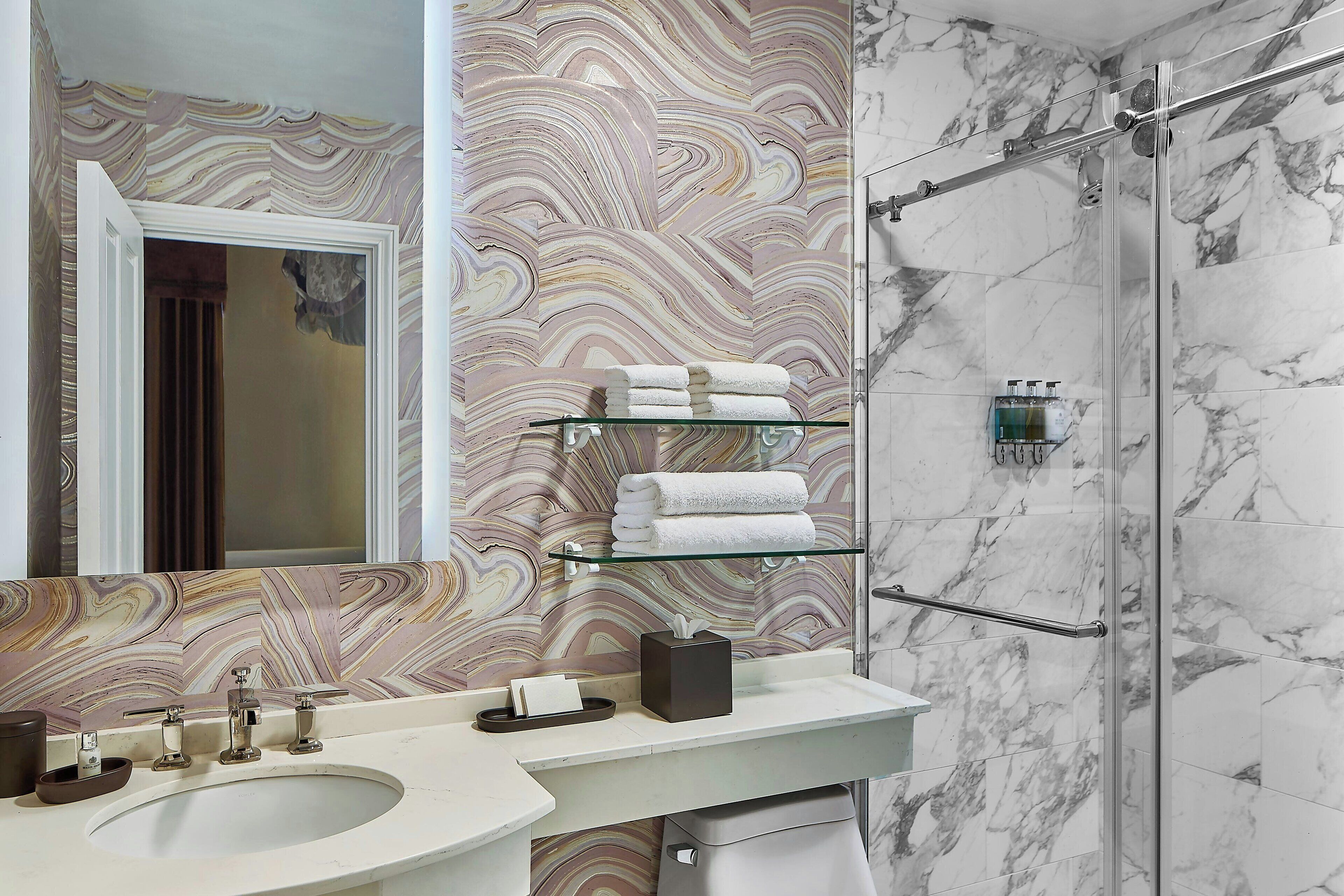 A bathroom with a marble shower, a glass sink, and a marble backsplash.