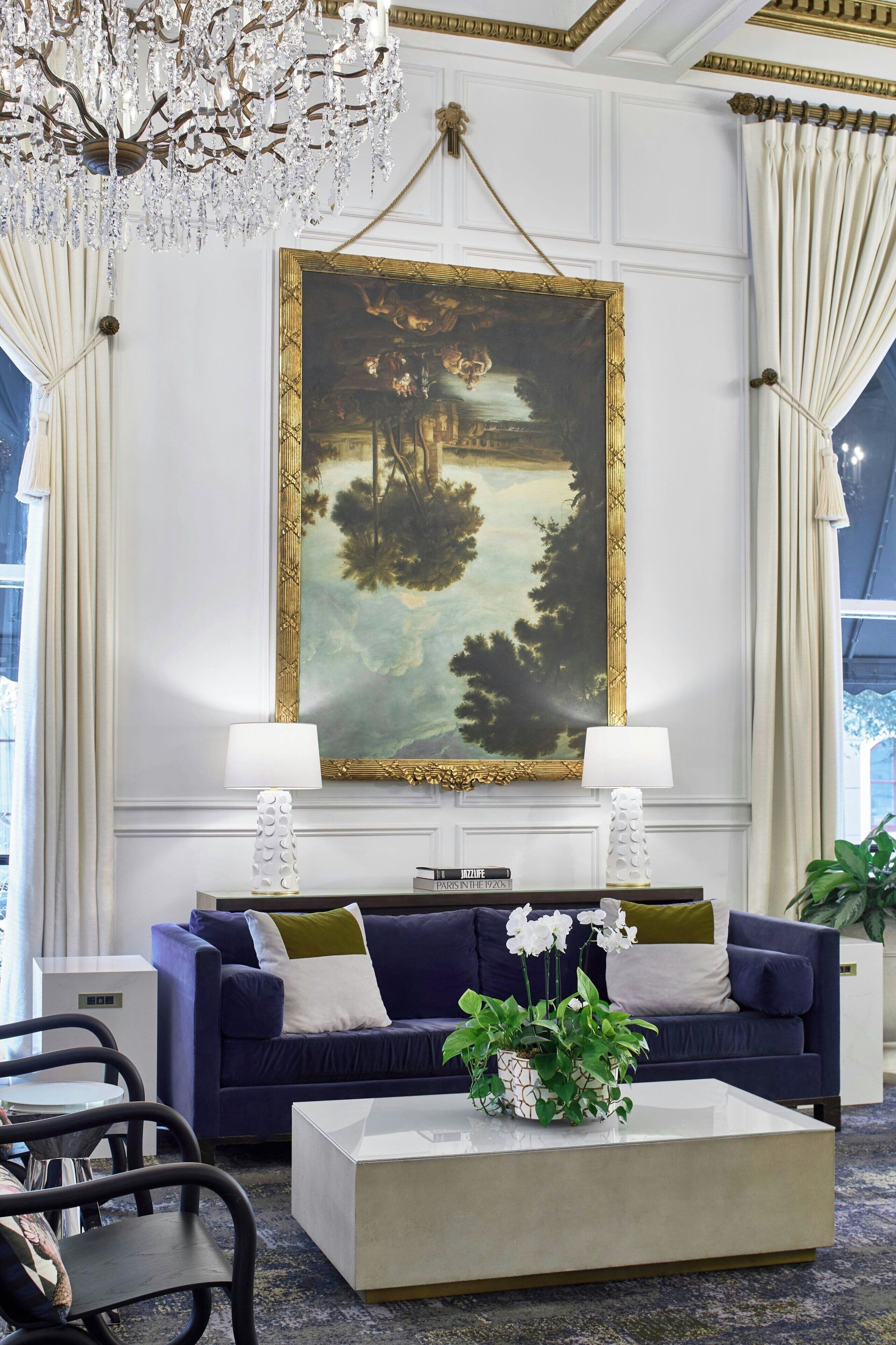 Une pièce décorée d’un grand tableau représentant un paysage, d’un canapé bleu, de deux lampes et d’une table basse sur laquelle est posée une plante.