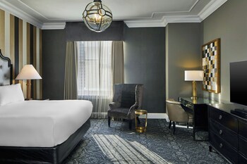 A room with two black sofas, a wooden chess table, a fireplace with a portrait above, and wall sconces. at Le Pavillon, New Orleans, a Tribute Portfolio Hotel by Marriott