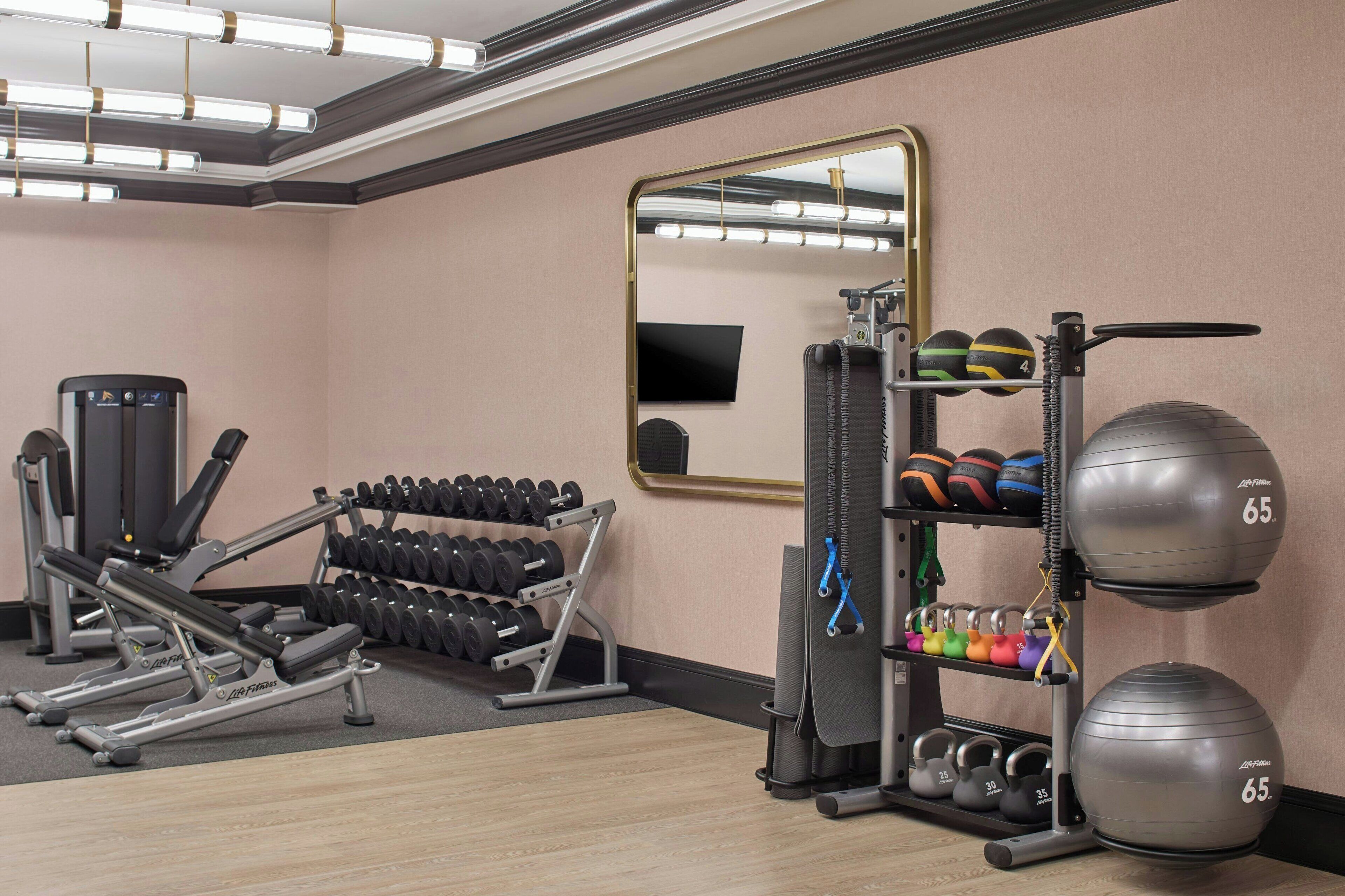 A gym with weightlifting equipment, dumbbells, and exercise balls.