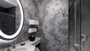 Une salle de bain dotée d’un grand miroir, d’un lavabo blanc, d’une cabine de douche en verre et d’un papier peint décoratif.