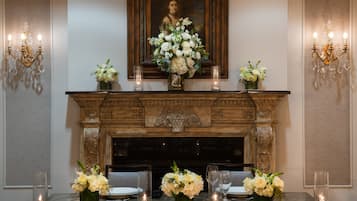 Comedor formal con chimenea, un retrato sobre ella y mesas preparadas para una comida a la luz de las velas.