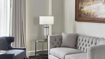 Una habitación con un sofá gris, un sillón azul, una mesita redonda, una lámpara de pie y un cuadro grande en la pared.