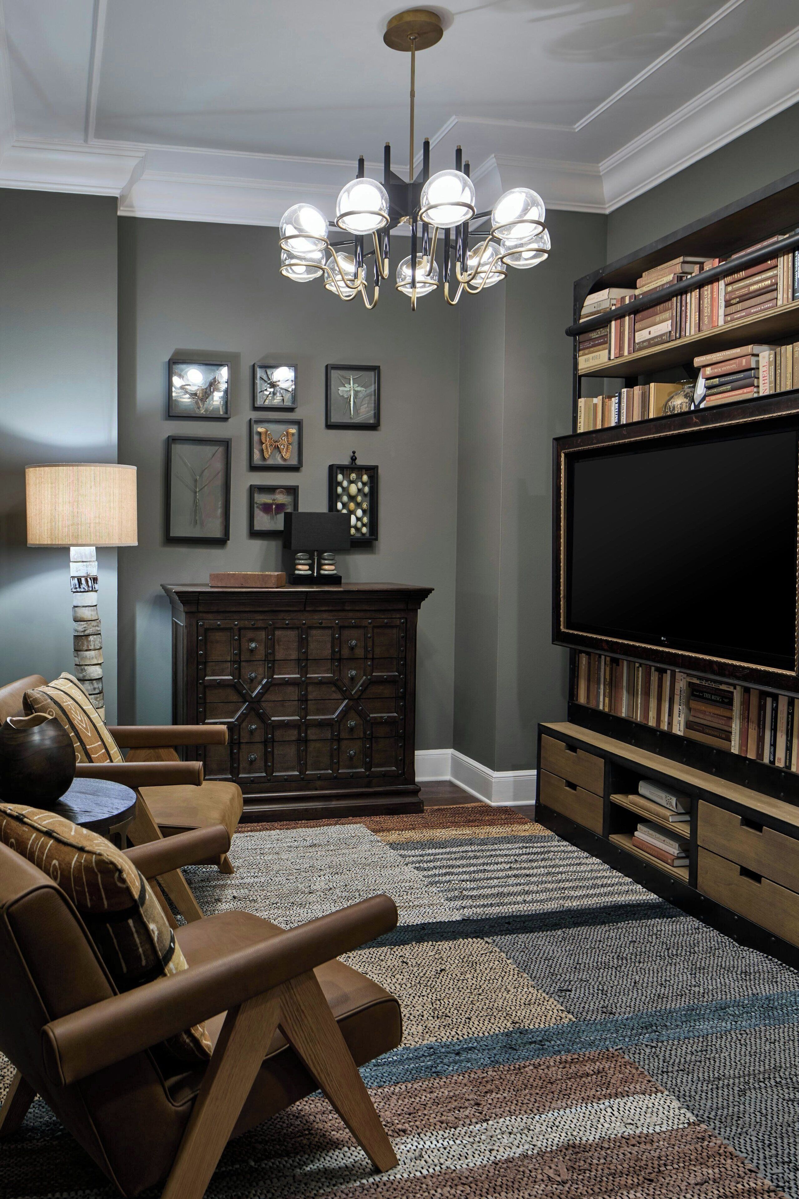 Un soggiorno con un mobile TV in legno scuro, un'ampia televisione a schermo piatto, un lampadario e un tappeto decorato.