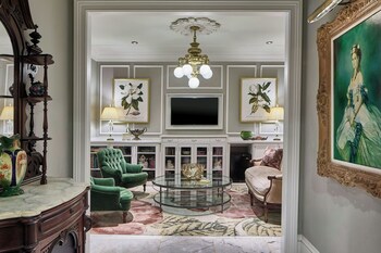 A bar area with red upholstered chairs, a bar counter with shelves of bottles, and a large painting on the wall. at Le Pavillon, New Orleans, a Tribute Portfolio Hotel by Marriott