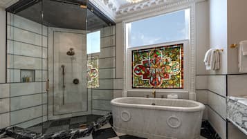 A luxurious bathroom with a freestanding bathtub, a glass-enclosed shower, and a stained glass window.