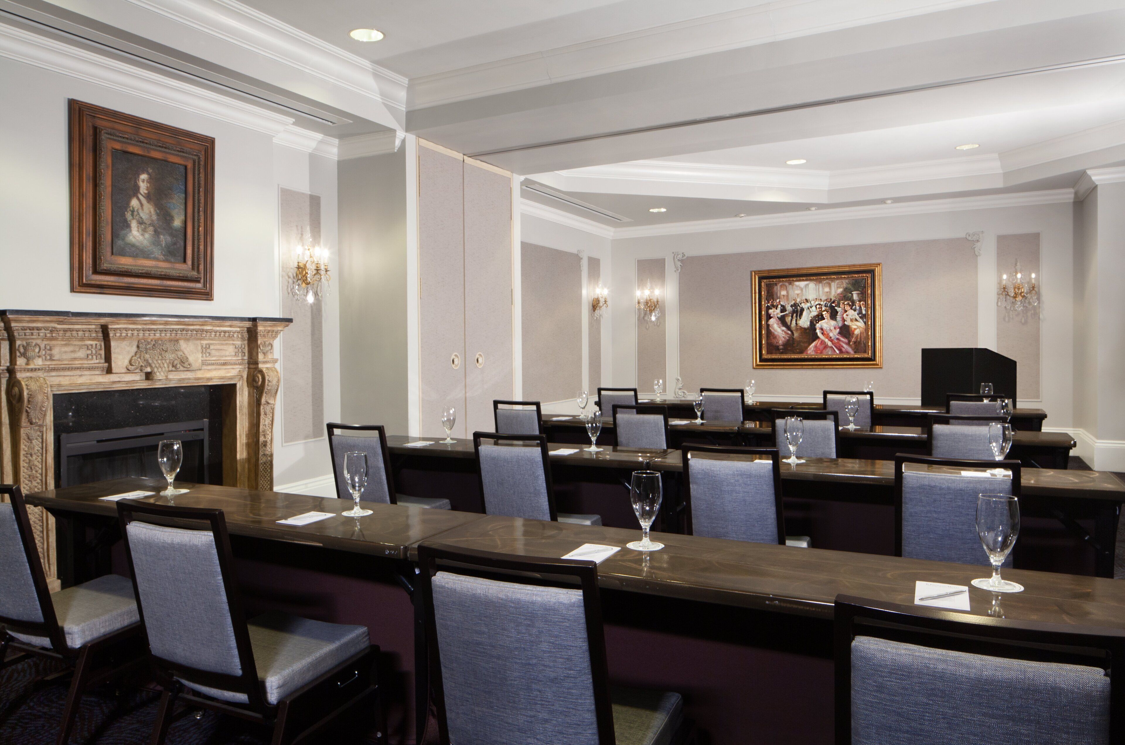 A conference room with a fireplace, a large painting, and multiple tables with chairs.