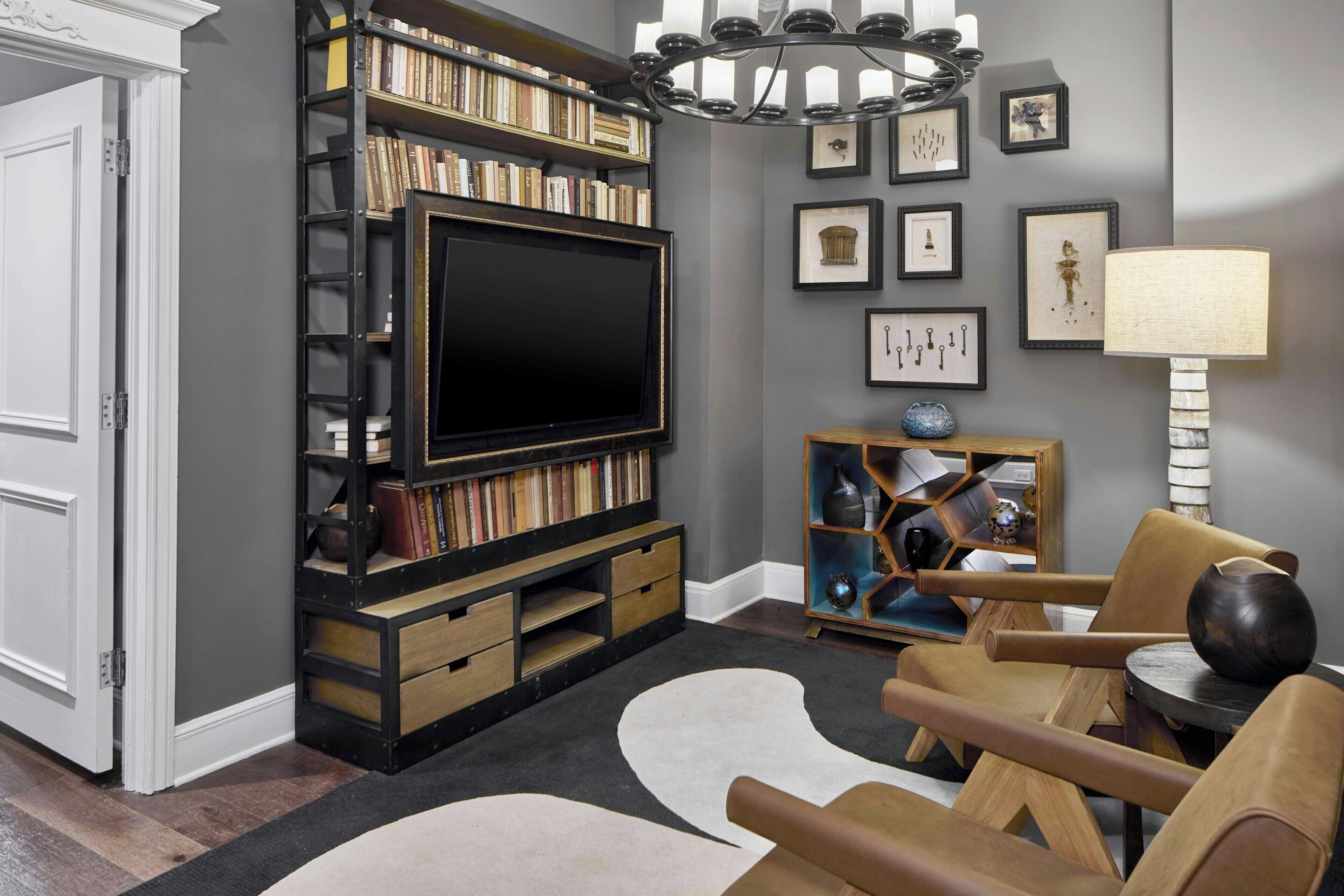 A living room with a large flat-screen TV, a bookshelf, a decorative lamp, and a modern chair.