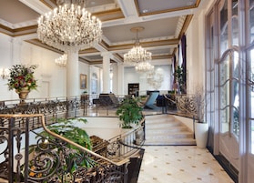 Un amplio vestíbulo con candelabros ornamentales, una escalera de mármol y una zona de estar con vistas a la ciudad.