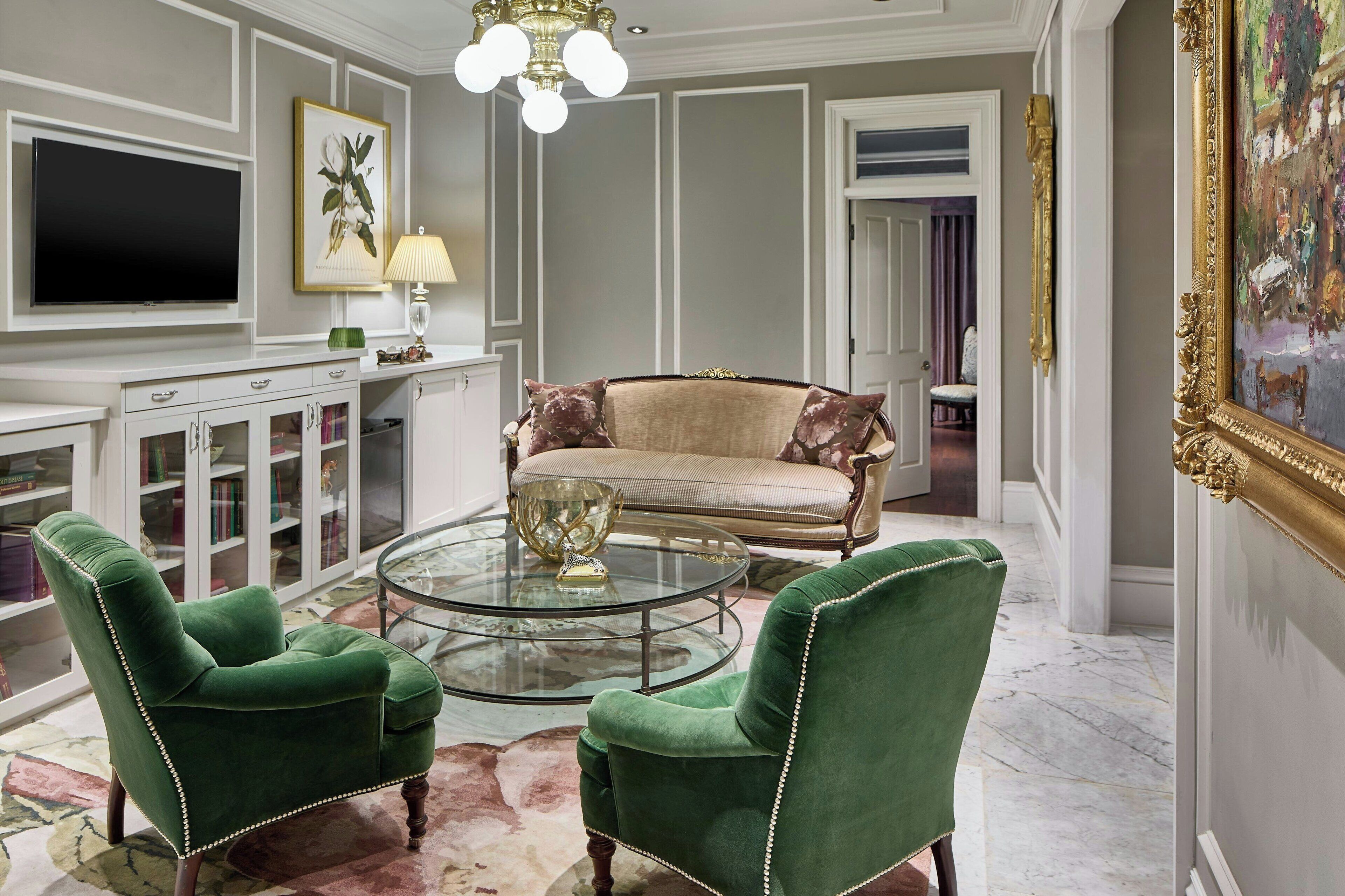 A living room with a green armchair, a sofa, a glass coffee table, a TV, a lamp, and a painting.